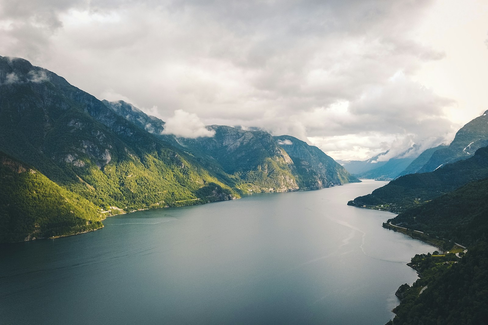 green mountains beside body of water under cloudy sky during daytime